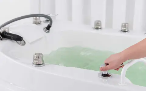 Dłoń reguluje strumień wody w wannie, przygotowując relaksujący masaż wirowy.
