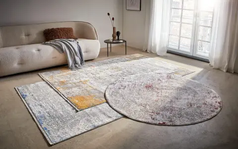 Mattor inspiration: En rund och två rektangulära mattor med abstrakt mönster i grått, vitt, gult och rött ligger på ett betonggolv framför en soffa.