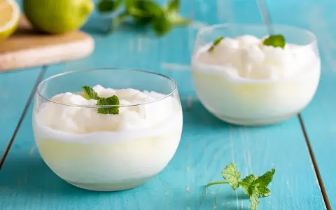 Due bicchieri di sorbetto al limone senza albume, guarniti con menta fresca, su un tavolo di legno blu.