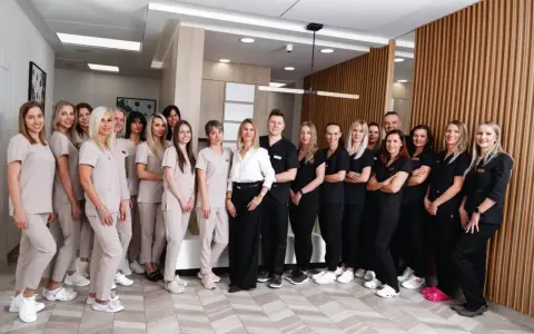 Grupa uśmiechniętych dentystów i personelu medycznego w jasnych i ciemnych uniformach stoi w nowoczesnym gabinecie.