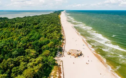 Majówka nad morzem: zielony las, piaszczysta plaża z kilkoma osobami i bunkrem w kamuflażu, szmaragdowe fale Bałtyku.