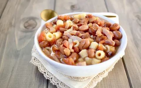 Una ciotola di pasta e fagioli in scatola, con pomodoro e pancetta, servita su un tovagliolo di pizzo.