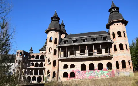 Niedokończony zamek z cegły z wieżami i graffiti na tle błękitnego nieba.