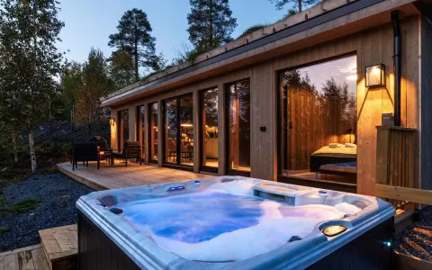 En bubblande badtunna framför en modern stuga i Norge. Trädäck, utemöbler och en grönskande takterrass skapar en mysig atmosfär.