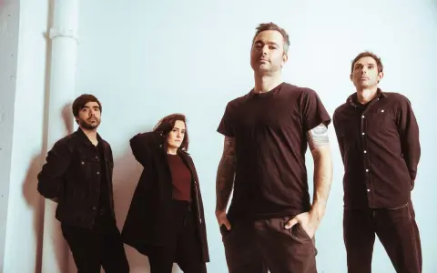 Quatre musiciens, un groupe rock canadien francophone, posent devant un mur blanc.