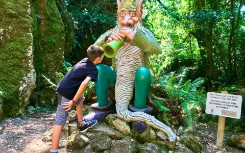 Un niño observa fascinado una figura de duende en un bosque de Cantabria con niños. ¡Una aventura mágica!