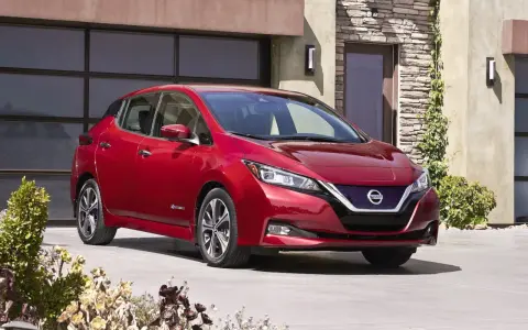 Czerwony Nissan Leaf przed nowoczesnym domem. Sprawdź atrakcyjną nissan leaf cena i wybierz swój wymarzony samochód elektryczny.