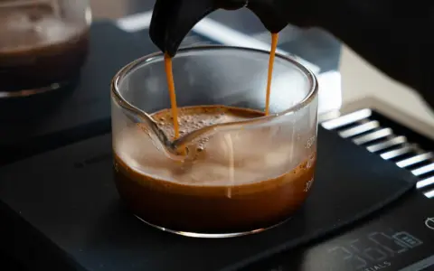 Frisch gebrühter Espresso fließt in ein Glasgefäß, die goldbraune crema de cafe bildet eine samtige Schicht.