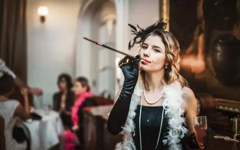 Kobieta w stylu lat 20. z cygaretką i piórami, na tle imprezy.