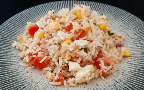 Une généreuse portion de salade de riz thon, garnie de dés de tomates, de maïs et d'œufs durs, sur une assiette texturée.