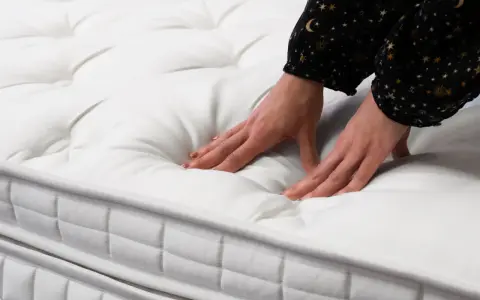 Mains testant la douceur d'un matelas blanc matelassé. Quel matelas pour mal de dos dur ou mou ? Le confort est essentiel.