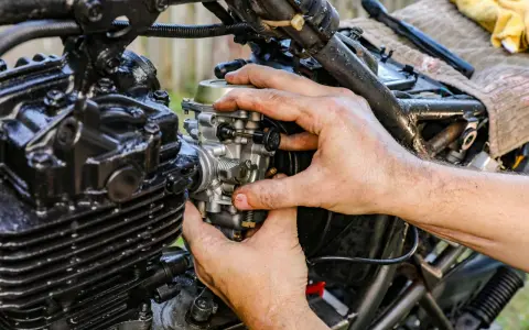 Ręce mechanika regulują gaźnik motocykla, pokazując, jak działa ssanie.