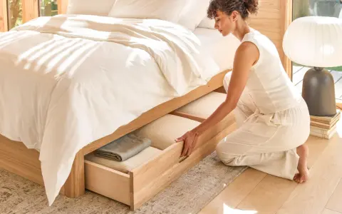 Une femme range des draps dans un tiroir de lit en bois.