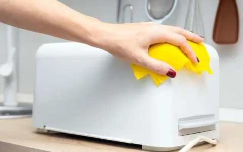 Eine Hand wischt mit einem gelben Tuch über einen weißen Toaster. So einfach ist das Toaster reinigen für ein blitzsauberes Ergebnis.