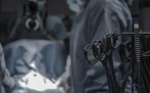 Narzędzia chirurgiczne w zbliżeniu. W tle niewyraźny zespół medyczny podczas procedury, która może być operacją lub zabiegiem.