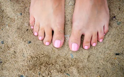 Stopy na piasku z różowym, modnym pedicure. Idealne na lato.