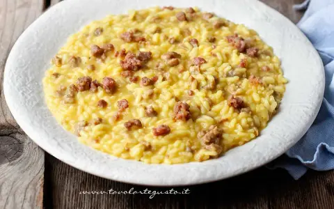 Un cremoso risotto con salsiccia, servito in un piatto bianco su un tavolo di legno rustico.