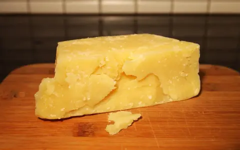 Kawałek żółtego sera typu Grana na drewnianej desce.