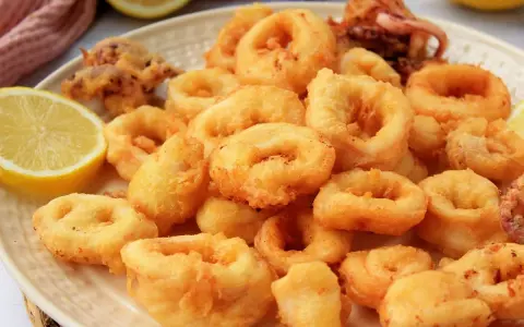 Plato de calamares a la romana dorados y crujientes, servidos con rodajas de limón fresco.