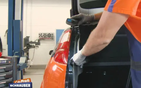 Ein Mechaniker wechselt das Bremslicht eines Ford Focus. Er hält ein Werkzeug in der Hand und arbeitet am Heck des Autos.