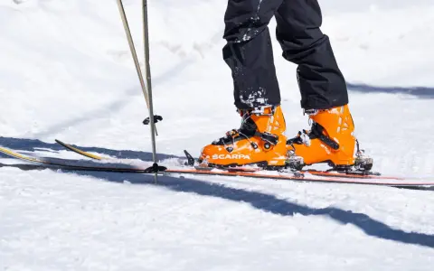 Pomarańczowe buty narciarskie Scarpa na nartach, z kijkami narciarskimi w śniegu.