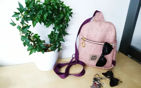 Sac à dos rose texturé, parfait pour une femme. Un patron sac à dos femme gratuit pour créer le vôtre. Lunettes de soleil et clés à proximité.