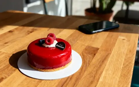 Un délicieux entremet fruit rouge, glacé et garni de framboises fraîches, attend sur une table en bois.