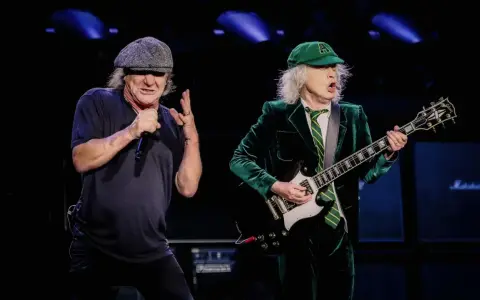 Brian Johnson i Angus Young, legendarny skład AC/DC, na scenie. Brian śpiewa do mikrofonu, Angus gra na gitarze.