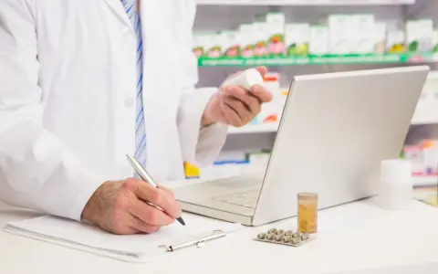 Farmaceuta sprawdza w komputerze pradaxa zamiennik, trzymając w dłoni buteleczkę leku.