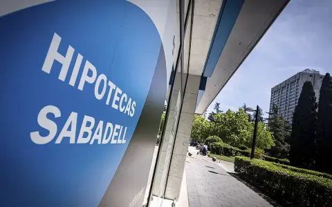 Letrero azul con "HIPOTECAS SABADELL" en blanco. Fachada de edificio moderno con vegetación y cielo azul.