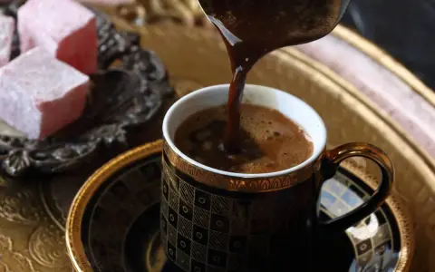 Gorąca, aromatyczna kawa, jedna z najmocniejszych kaw, nalewana do ozdobnej filiżanki. Obok słodkie lokum.