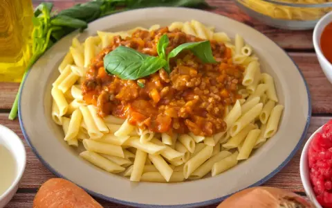 Plato de macarrones a la boloñesa, con salsa de carne y tomate, decorado con hojas de albahaca fresca.