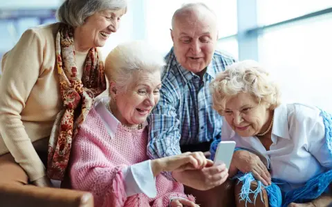 Cztery starsze osoby śmieją się, patrząc na telefon. Może sprawdzają, jak sprawdzić nfz kolejka do sanatorium?