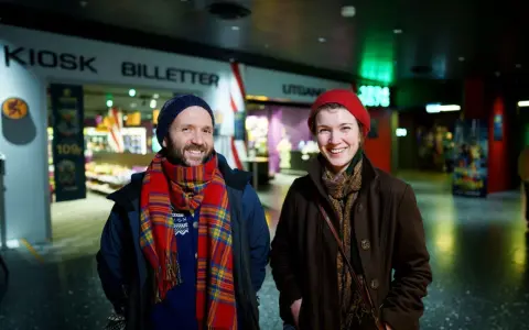Två glada personer vid en biljettkiosk, redo att se filmer på bio nu.