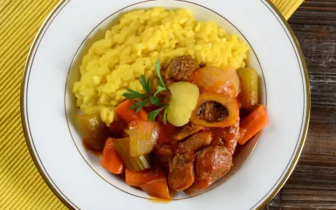 Risotto giallo e ossobuco con verdure, un classico dei piatti tipici milanesi, guarnito con prezzemolo e scorza di limone.