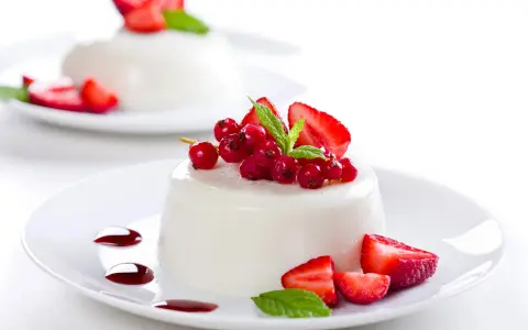 Deliciosa panna cotta cremosa adornada con fresas, grosellas rojas y menta fresca.
