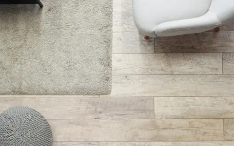 Elige el color del suelo de una casa con este suelo de madera clara, alfombra beige y puf gris.