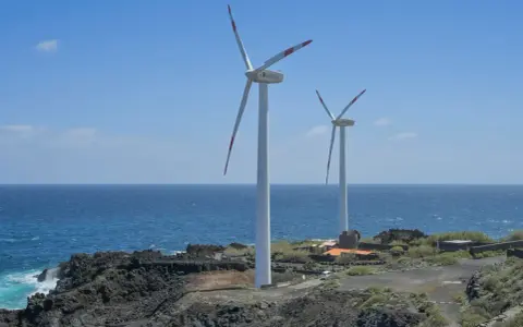 Zwei Windräder stehen an einer felsigen Küste Spaniens. Sie sind Teil des Strommixes und erzeugen saubere Energie.
