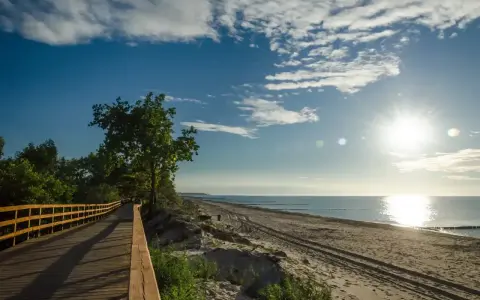 Drewniana ścieżka wzdłuż plaży, idealna na przejażdżkę rowerem po trasie rowerowej R10. Słońce odbija się w morzu.