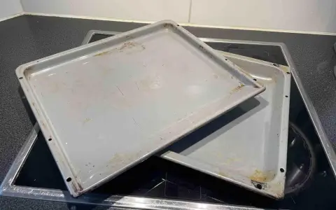 Zwei eingebrannte Backbleche liegen auf einem Cerankochfeld. Zeit, sie zu reinigen und wieder glänzen zu lassen!