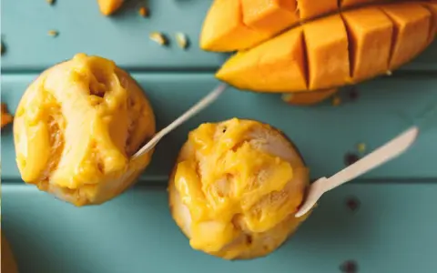 Jak zrobić sorbet? Dwa pucharki z mango sorbetem i kawałki świeżego mango na turkusowym tle.