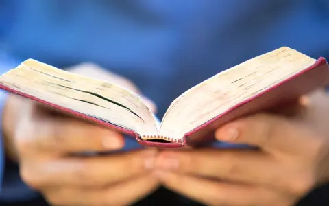 Otwarta księga z czerwonym grzbietem, trzymana w dłoniach. Może zawierać 10 przykazań bożych dla dzieci.