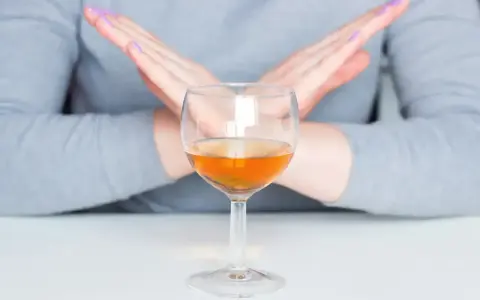 Ręce skrzyżowane nad kieliszkiem z bursztynowym płynem. Pytanie: po jakim czasie od zastrzyku można pić alkohol?