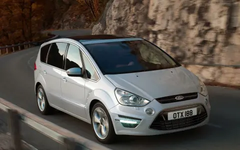 Biały Ford S-Max 2.0 TDCI pokonuje zakręt na malowniczej drodze wśród jesiennych drzew i skał.
