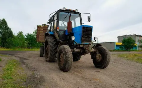 Niebieski traktor z przyczepą na tle wiejskiego krajobrazu. Zastanawiasz się, ile zarabia traktorzysta?