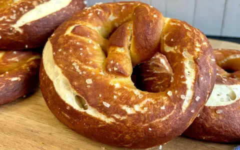 Frisch gebackene, goldbraune sauerteig brezeln mit grobem Salz bestreut, liegen auf einem Holzbrett.