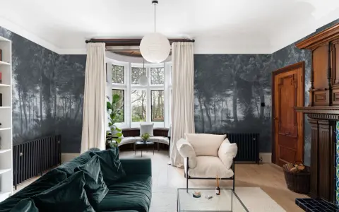 Sala con papel pintado de bosque, sofá verde, sillón beige y chimenea de madera. Ideas de como poner papel pintado para transformar tu hogar.