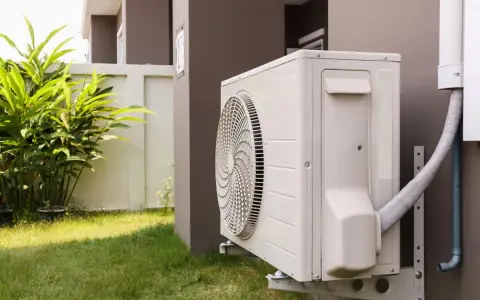 Unité extérieure de pompe à chaleur avec tuyau pour l'évacuation eau condensation. L'appareil est fixé au mur d'une maison, près d'une pelouse et de végétation.