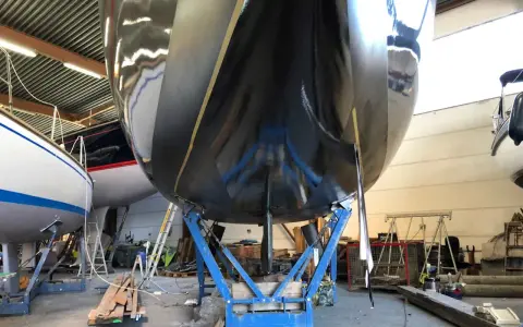 Schwarzer Bootsrumpf auf Stützen, bereit für den antifouling test. Glänzende Oberfläche reflektiert die Werkstatt.