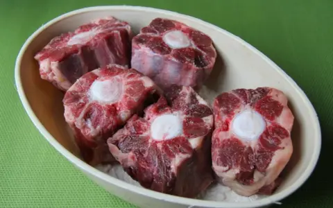 Trozo de rabo de ternera crudo en un cuenco, con el hueso central visible.